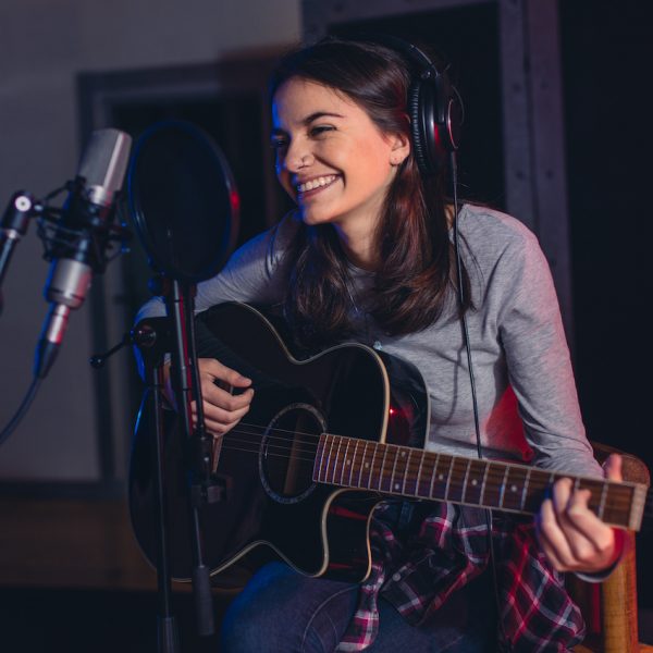 Female singer playing guitar and singing a song. Woman performing in a recording studio. Recording for her album.